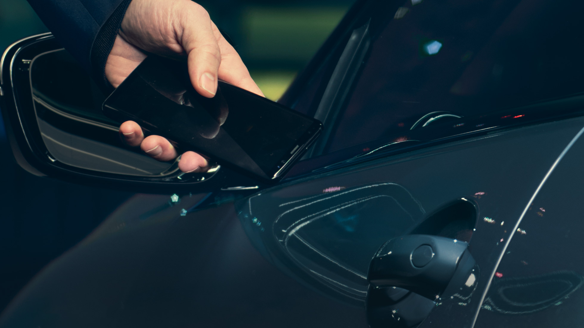 Digitālā atslēga Digitālā atslēga: Vīrietis automobiļa ārpusē pie tā durvīm tur viedtālruni