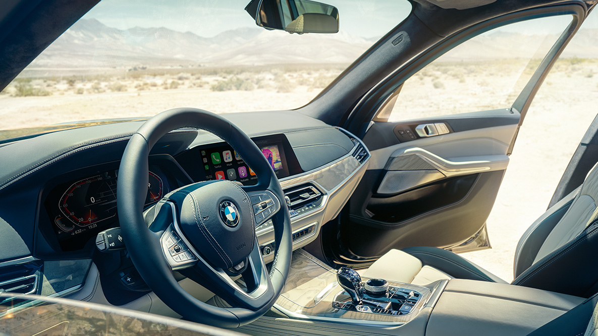 BMW X7 salons BMW X7 salons: skats no ārpuses uz pirmo sēdekļu rindu ar stūri, instrumentu paneli un ādas sēdekļiem
