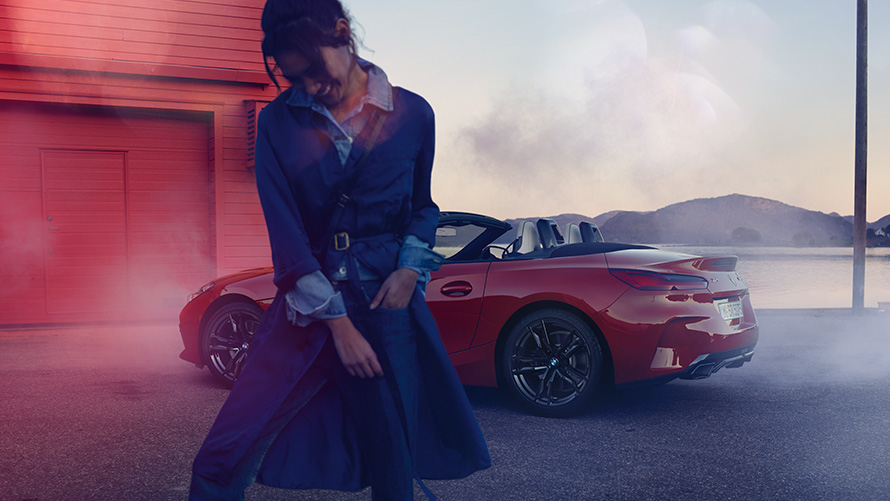 BMW Z4 M40i Roadster G29, ar nolaistu mīkstā seguma jumtu BMW Z4 M40i Roadster G29, trīs ceturtdaļu aizmugures skats ar nolaistu mīkstā seguma jumtu un sievieti priekšplānā