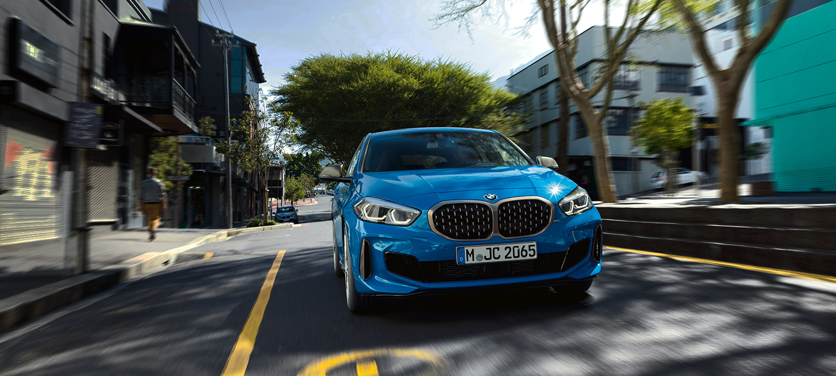 BMW 1. sērijas metāliskā Misano Blue krāsā, braucošs automobilis no priekšpuses.