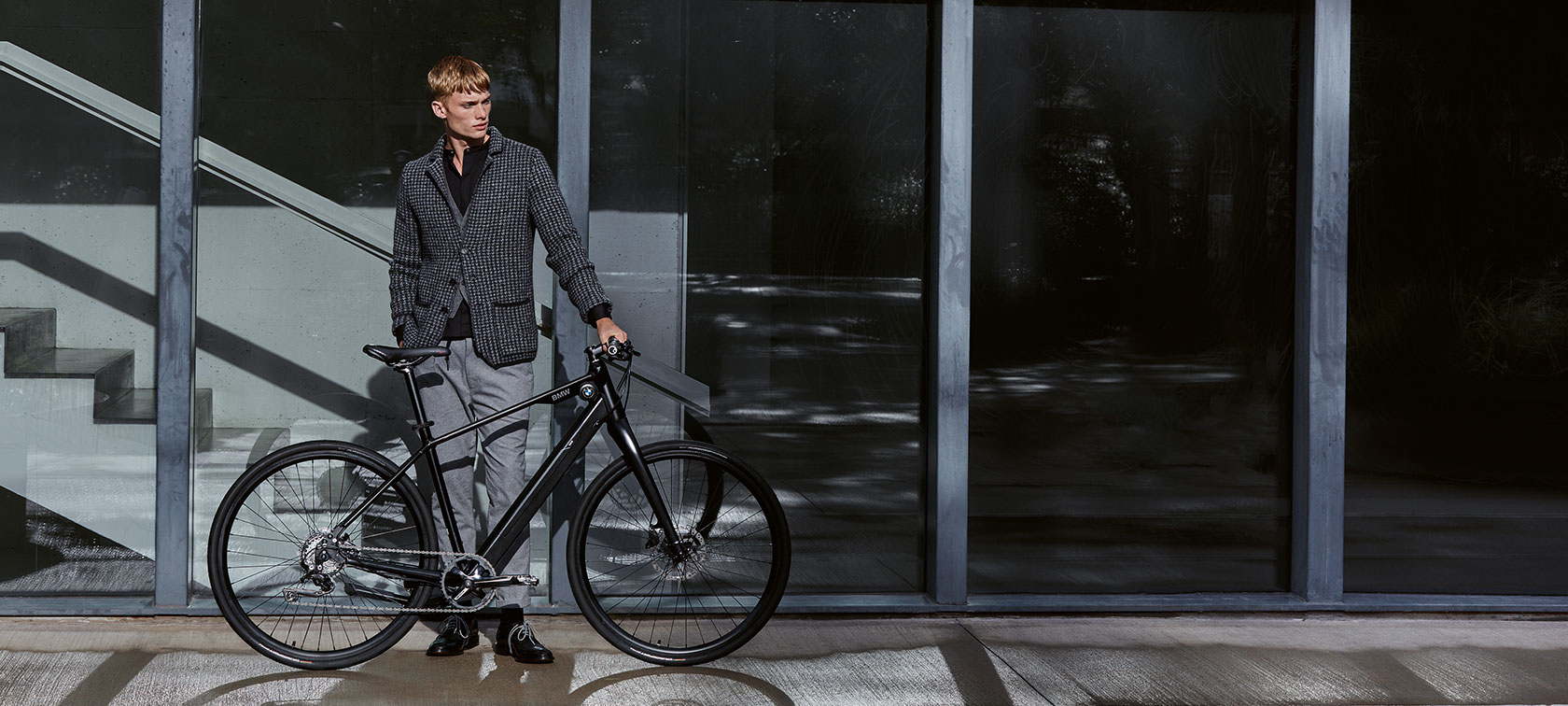Dizains un funkcija. Vīrietis stāv ikdienišķā pozā blakus BMW Urban Hybrid E-Bike.