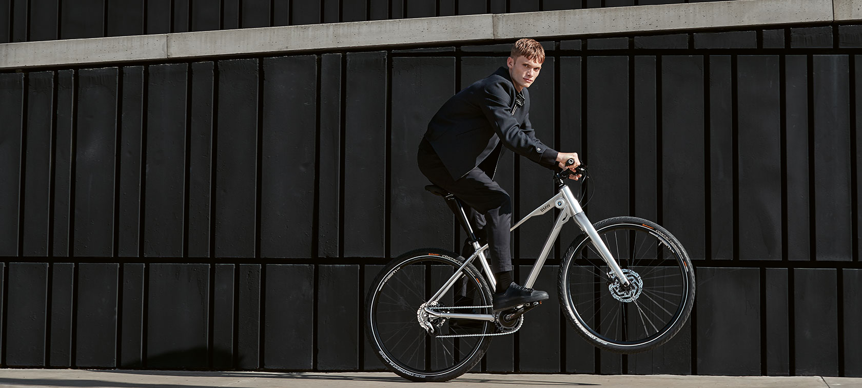 BMW velosipēdi. Šajā attēlā parādīts jauns vīrietis, kurš veic triku, braukdams tikai uz BMW Cruise velosipēda aizmugurējā riteņa.