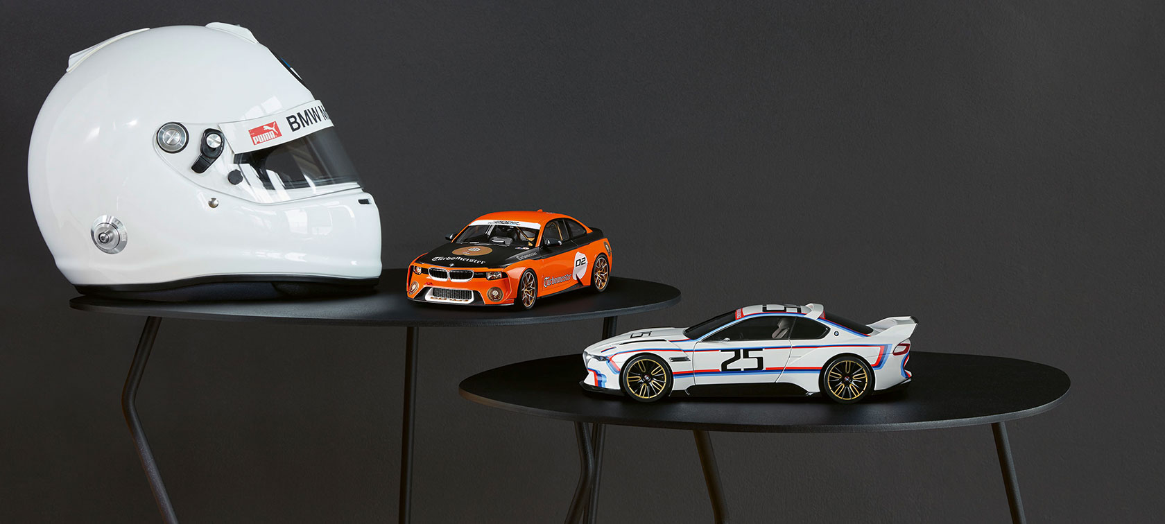 Attēlā BMW 2002 Homage Turbomeister miniatūra un BMW 3.0 CSL 25 miniatūra izvietotas pa labi, blakus baltajai ķiverei. Attēlā BMW 2002 Homage Turbomeister miniatūra un BMW 3.0 CSL 25 miniatūra izvietotas pa labi, blakus baltajai ķiverei.