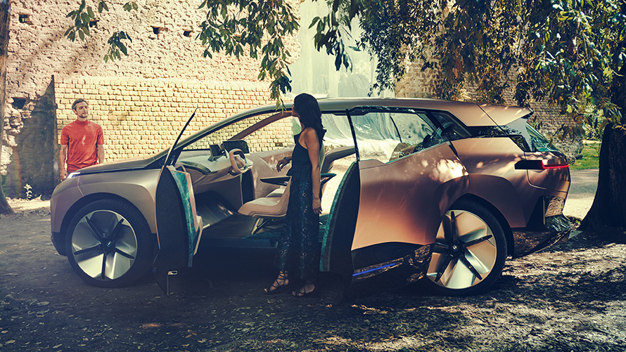 BMW Vision iNEXT no sāna BMW Vision iNEXT no sāna ar sievieti un atvērtām durvīm un vīrieti fonā