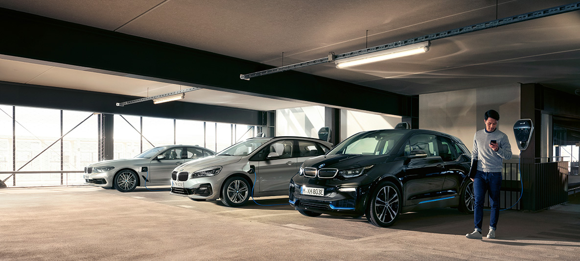 BMW elektroautomobiļi un hibrīdauto uzlādes stacijā BMW nodokļu atvieglojumi, BMW elektroautomobiļi un hibrīdauto, vīrietis uzlādes stacijā