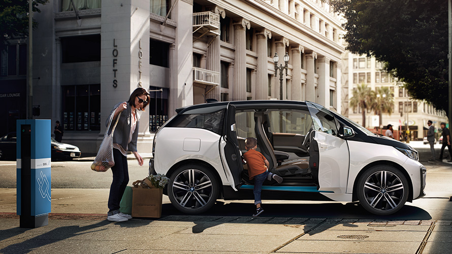 BMW i3 uz pilsētas fona BMW klāsts, BMW i3 uz pilsētas fona ar sievieti un bērnu
