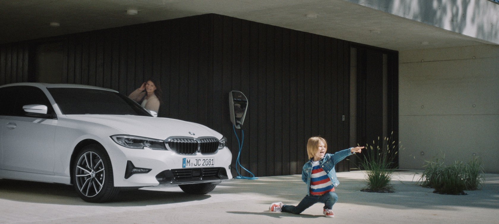 BMW hibrīdauto uzlādes stacijā BMW hibrīdauto, zēns uz BMW hibrīdauto fona uzlādes stacijā