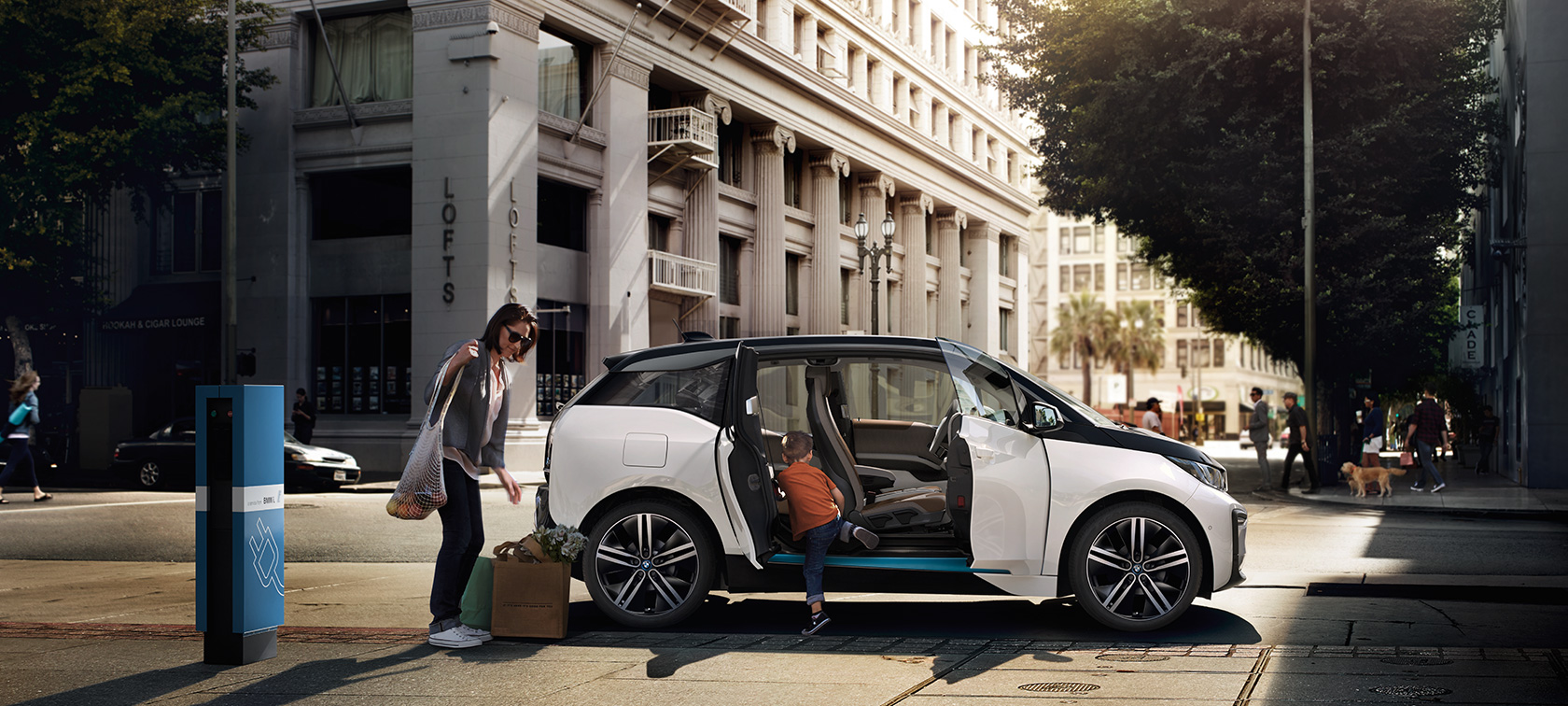 BMW i3 uz pilsētas fona BMW klāsts, BMW i3 uz pilsētas fona ar sievieti un bērnu