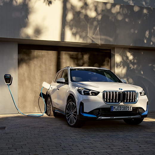 BMW iX1, U11, BEV, uzlāde procesā uz garāžas fona