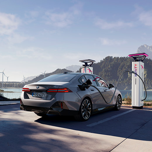 BMW i5 eDrive40, G60, uzlādes stacijā uz ezera fona