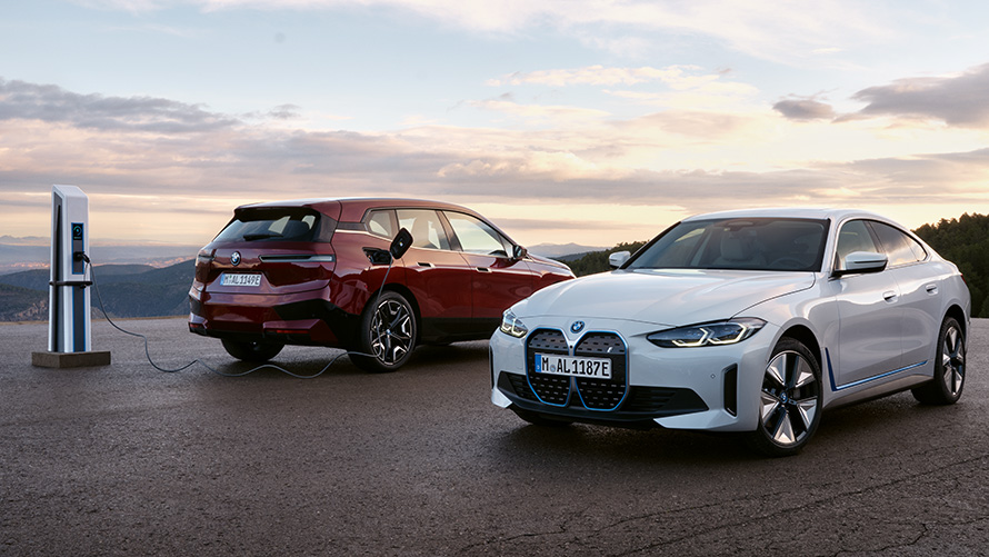 BMW BEV darbības attālums, BMW ilgtspēja BMW ilgtspēja, BMW BEV darbības attālums, divi BMW automobiļi stāv blakus uzlādes stacijai