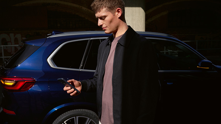 BMW digitālā atslēga – uzstādīta līdz pieciem lietotājiem BMW digitālā atslēga, uzstādīta līdz pieciem lietotājiem, vīrietis ar viedtālruni uz BMW X5 fona