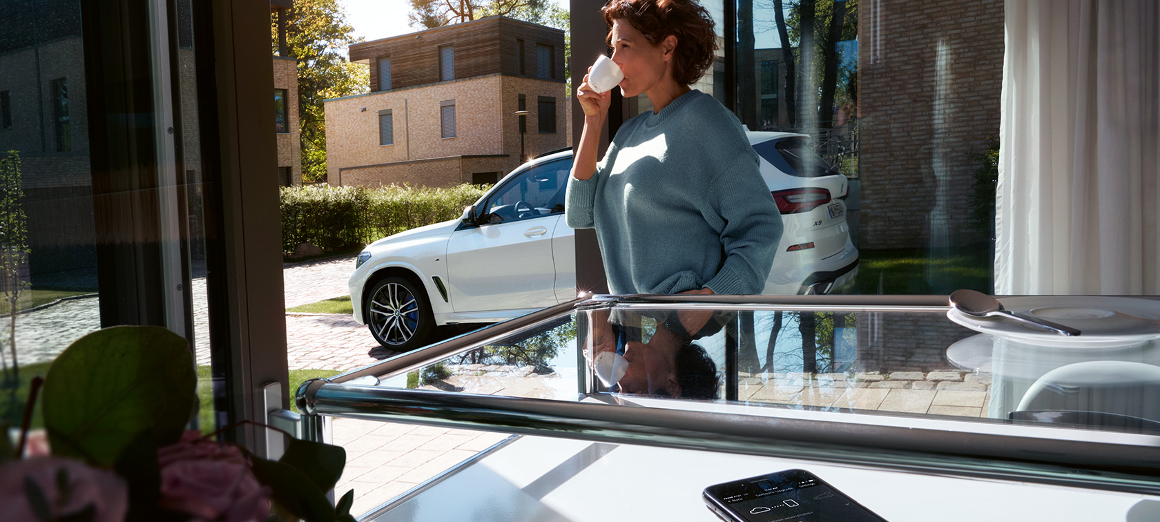 BMW attālā programmatūras jaunināšana Sieviete dzer no tasītes, kamēr BMW attālā programmatūras jaunināšana atjaunina viņas BMW X5 programmatūru