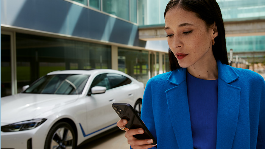 Sieviete stāv uz BMW fona Sieviete stāv BMW priekšā un skatās viedtālrunī