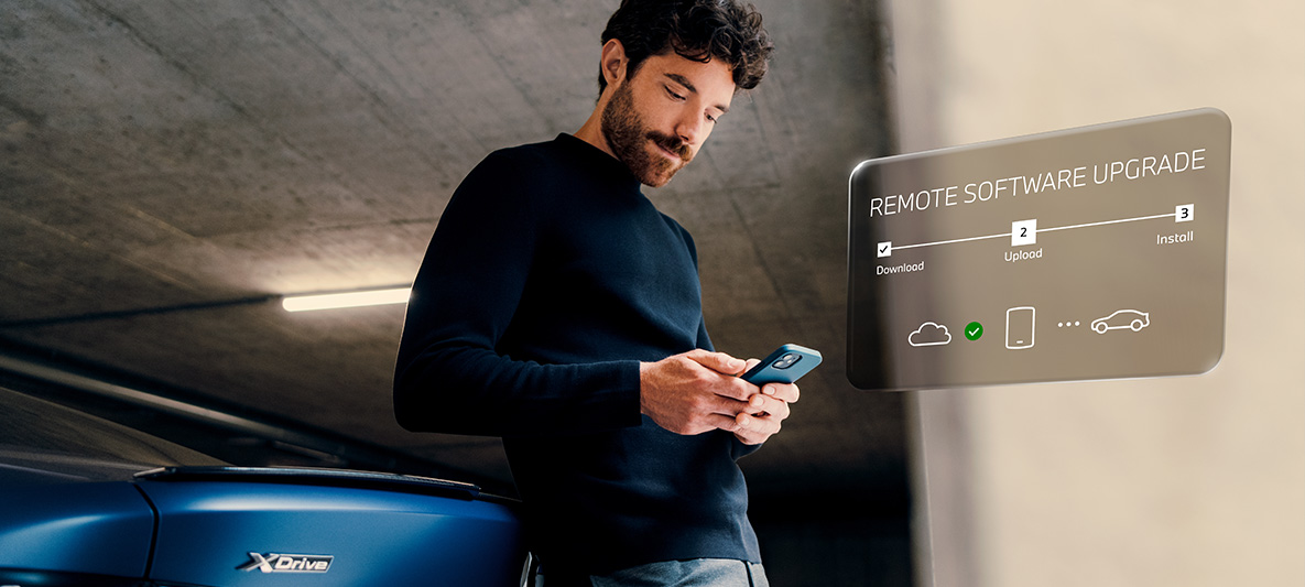 Vīrietis, atbalstījies pret BMW aizmuguri, skatās viedtālrunī Attālā programmatūras jaunināšana, vīrietis, atbalstījies pret BMW aizmuguri, skatās viedtālrunī