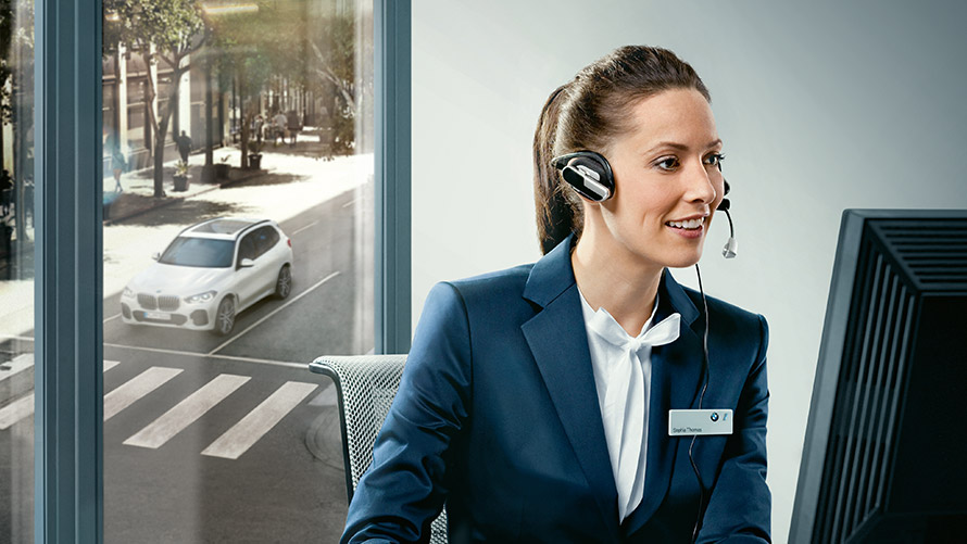 Concierge pakalpojumi Concierge pakalpojumi. BMW darbiniece ar austiņām sēž pie sava darba galda