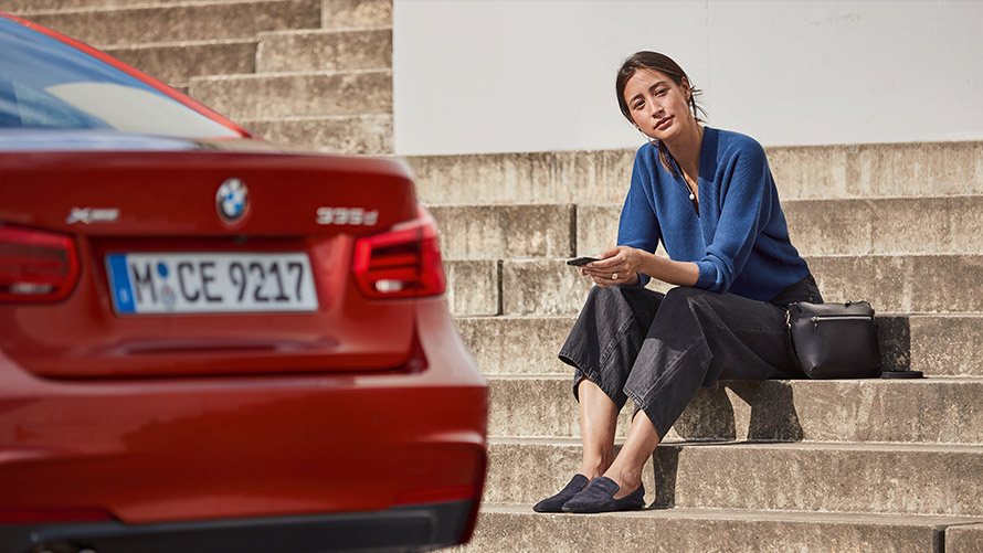 Palīdzība apkopes un avārijas gadījumā Sieviete sēž sava BMW priekšā un izmanto palīdzību apkopes un avārijas gadījumā