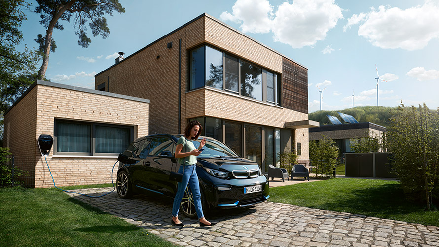 Digitālais uzlādes pakalpojums Sieviete iziet ārpusē sava BMW i3 priekšā un savā viedtālrunī izmanto digitālo uzlādes pakalpojumu