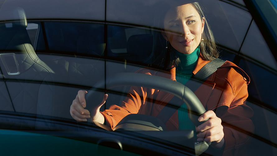 Sieviete pie BMW stūres Sieviete oranžā jakā pie BMW stūres