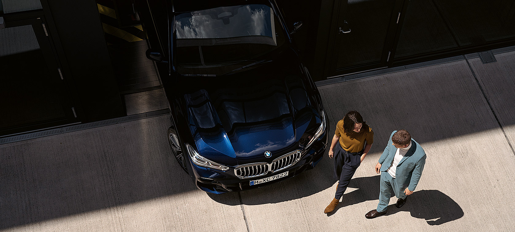 Sieviete un vīrietis iet garām BMW priekšdaļai Sieviete un vīrietis iet garām BMW priekšdaļai, skats no putna lidojuma