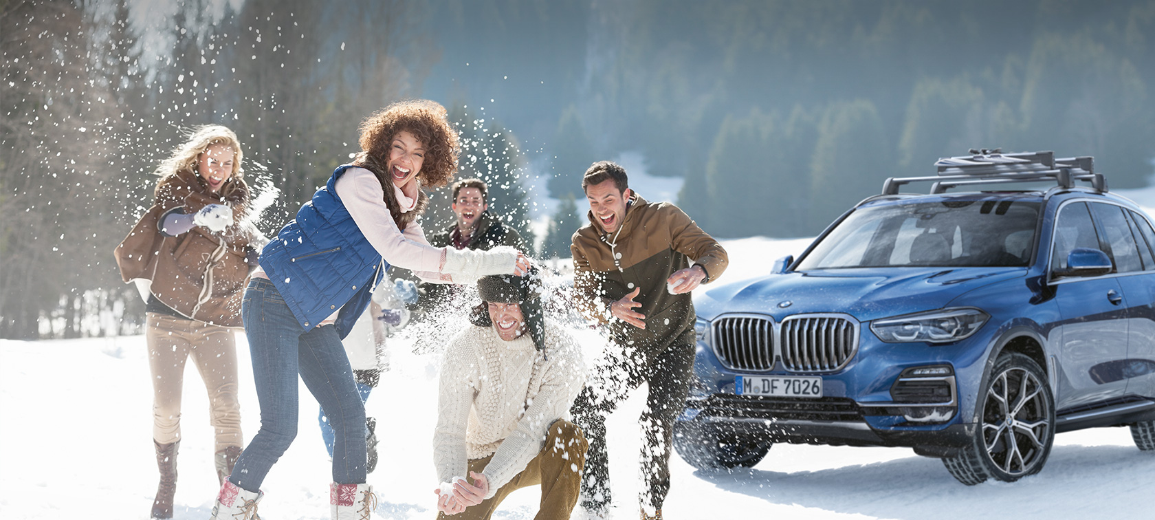 Oriģinālie BMW piederumi un BMW serviss rudenim un ziemai Sieviete un vīrietis smejas sniegā uz BMW fona