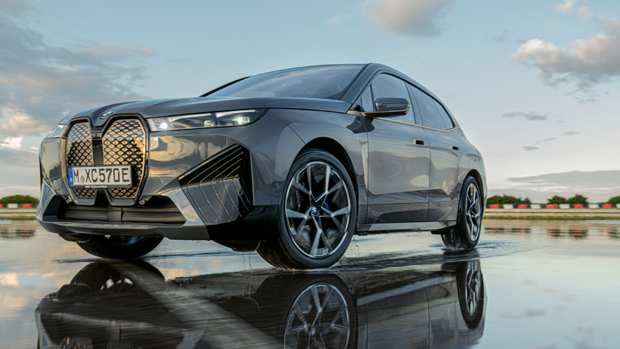 BMW diski, trīs ceturtdaļu priekšpuses skats uz BMW iX (i20) uz slapjas ielas BMW diski, trīs ceturtdaļu priekšpuses skats uz BMW iX (i20) uz slapjas ielas