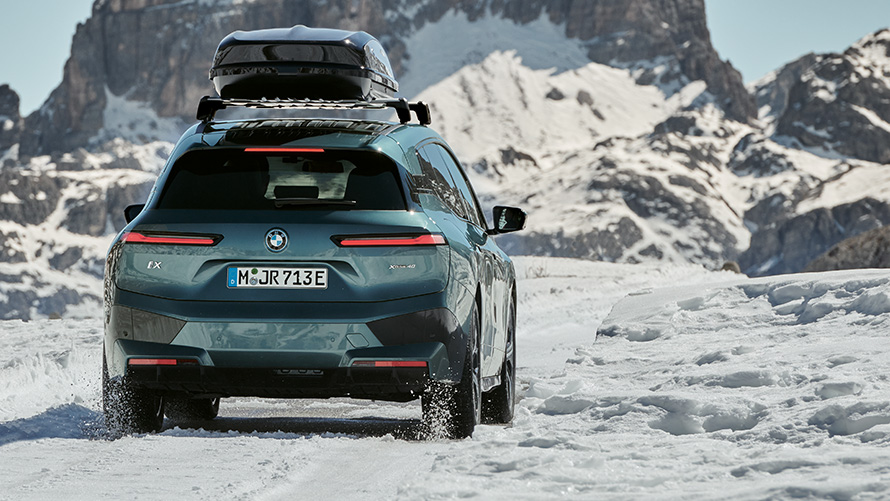 Nokomplektētie riteņi BMW Winter BMW iX (I20) uz sniega klāta ceļa ar kalniem fonā Nokomplektētie riteņi BMW Winter BMW iX (I20) uz sniega klāta ceļa ar kalniem fonā