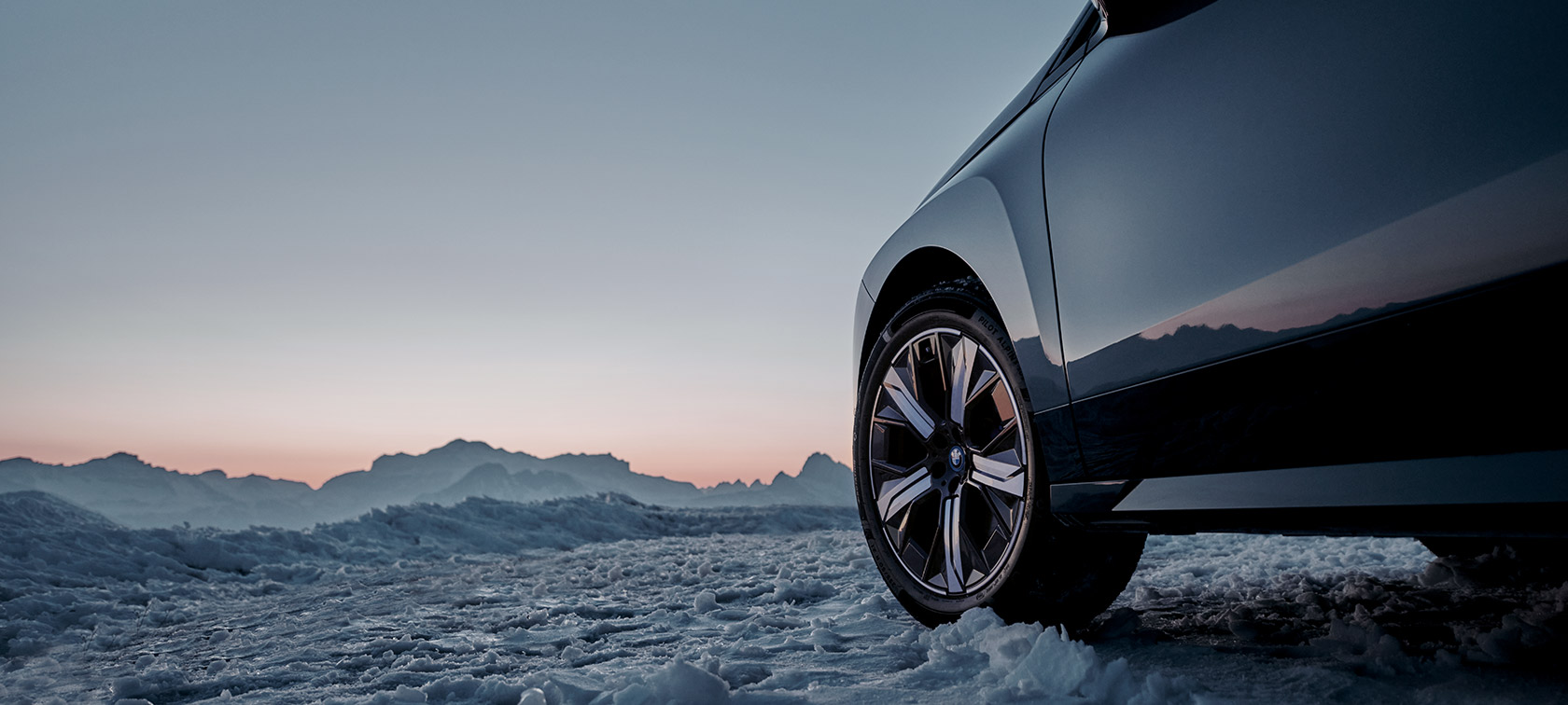 Oriģinālie BMW riteņi BMW iX (I20) sniegā uz kalnu fona Oriģinālie BMW riteņi BMW iX (I20) sniegā uz kalnu fona