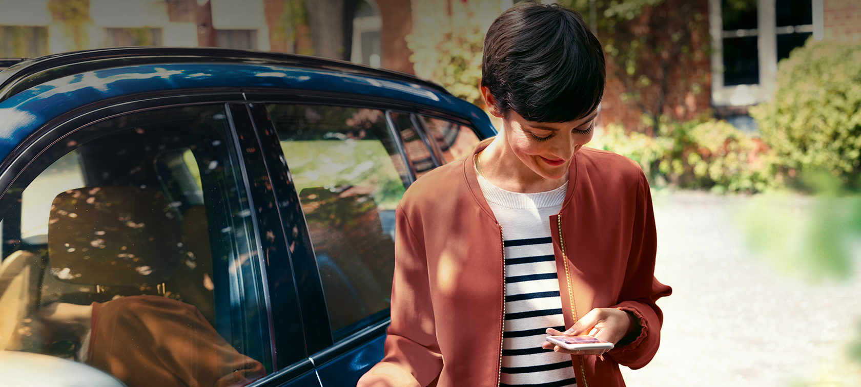 BMW Teleservices, sieviete skatās savā viedtālrunī BMW Teleservices, sieviete BMW priekšā skatās savā viedtālrunī